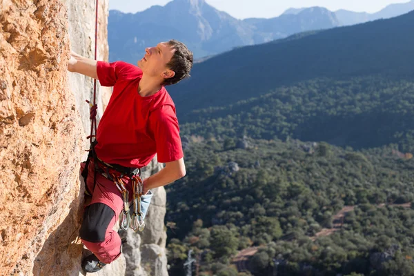 Junger Mann klettert auf Felswand in einem Tal mit Bergen bei Sonnenaufgang. — Stockfoto