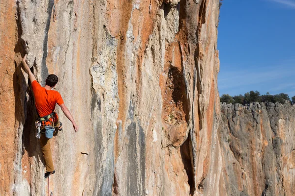 Young man climbs on a rocky wall in a valley with mountains at sunrise. — Stock Photo, Image