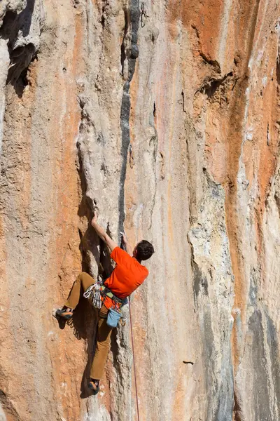 Mladý muž šplhá na skalnatou stěnu v údolí s horami za úsvitu. — Stock fotografie
