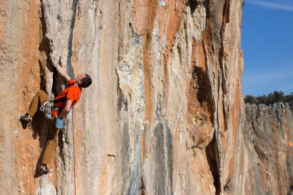 Νεαρός σκαρφαλώνει σε ένα βραχώδη τοίχο σε μια κοιλάδα με βουνά την ανατολή του ηλίου. — Φωτογραφία Αρχείου