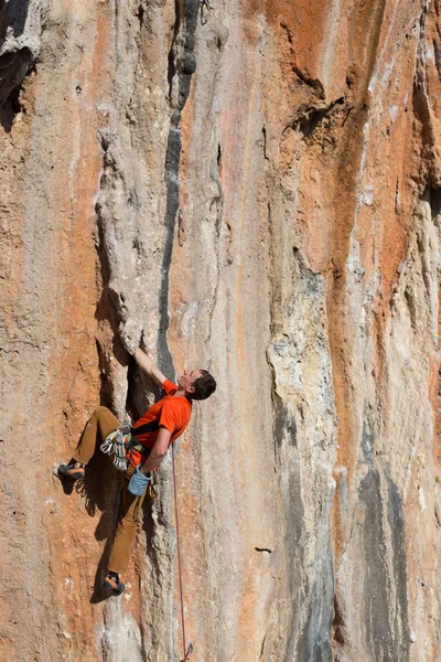 Joven sube a una pared rocosa en un valle con montañas al amanecer. — Foto de Stock