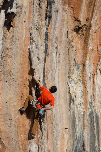 Νεαρός σκαρφαλώνει σε ένα βραχώδη τοίχο σε μια κοιλάδα με βουνά την ανατολή του ηλίου. — Φωτογραφία Αρχείου