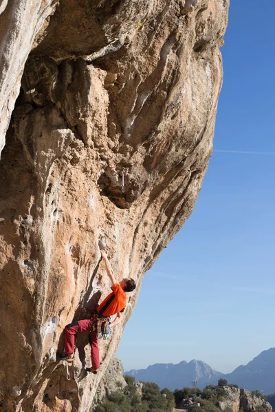 Unge man klättrar på en klippvägg i en dal med berg vid soluppgången. — Stockfoto