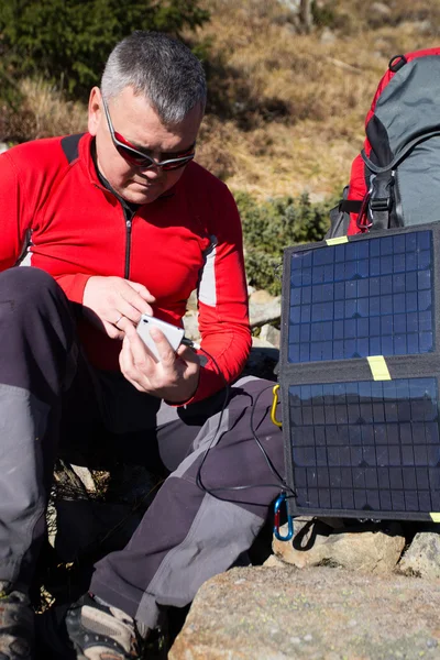 El panel solar unido a la carpa. El hombre sentado al lado del teléfono móvil carga desde el sol . — Foto de Stock