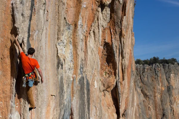 Young man climbs on a rocky wall in a valley with mountains at sunrise. — Stock Photo, Image