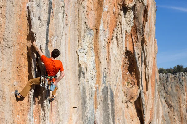 Joven sube a una pared rocosa en un valle con montañas al amanecer. — Foto de Stock