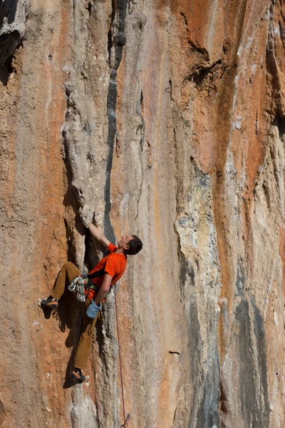 Joven sube a una pared rocosa en un valle con montañas al amanecer. — Foto de Stock