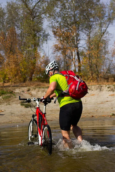 Young athlete crossing rocky terrain with bicycle in his hands. — Stock Photo, Image