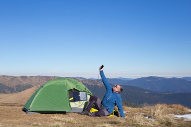 Çadır için bağlı güneş paneli. Güneş'ten cep telefon ücretleri yanında oturan adam.