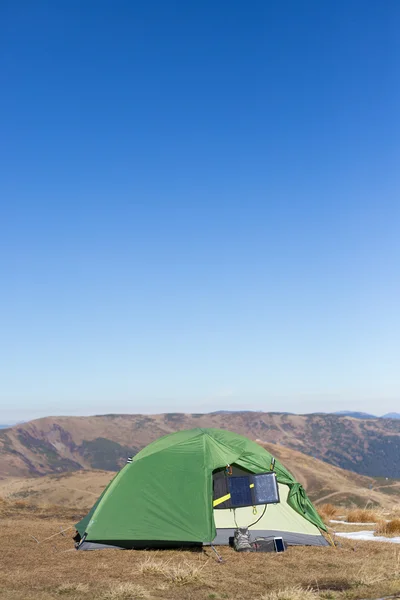 O painel solar ligado à tenda. O homem sentado ao lado das cargas do telefone móvel do sol . — Fotografia de Stock