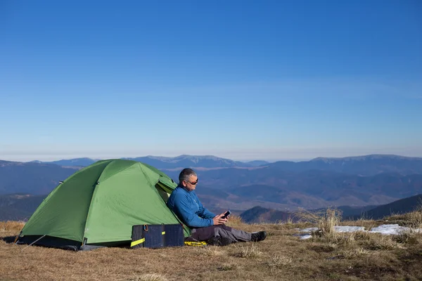 텐트에 부착 된 태양 전지 패널입니다. 태양에서 휴대 전화 요금 옆에 앉아 남자. — 스톡 사진