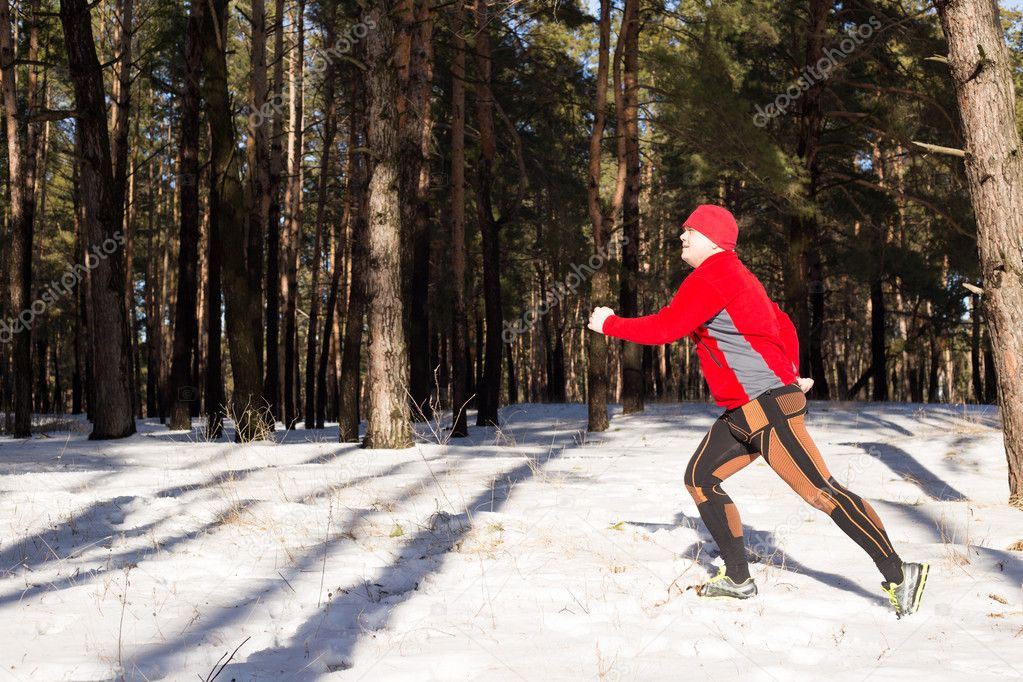 Winter trail running: man takes a run on a snowy mountain path in a pine woods.