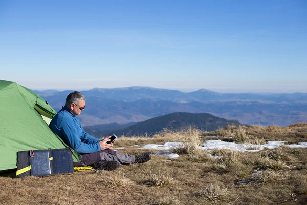 Die Solarzelle, die am Zelt befestigt ist. Der Mann sitzt neben Handyladungen von der Sonne. — Stockfoto