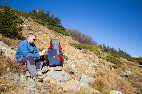 Die Solarzelle, die am Zelt befestigt ist. Der Mann sitzt neben Handyladungen von der Sonne. — Stockfoto