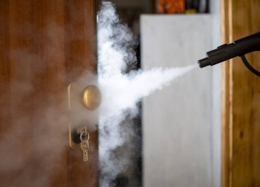 disinfection and sanitization with steam at home, steam flow is directed to the door handle and keys in the lock clipart