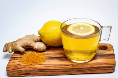 limon, zencefil, zerdeçal ve beyaz arka planda zeytin tahtasında bir bardak limon çayı.