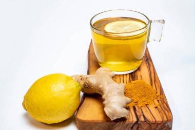 limon, zencefil, zerdeçal ve beyaz arka planda zeytin tahtasında bir bardak limon çayı.