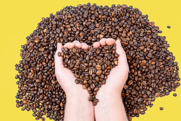 coffee beans close-up on the palm in the shape of a heart against the background of other coffee beans