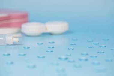 Su damlaları ile mavi arkaplan üzerinde kontak lensler, çanta ve araçlar