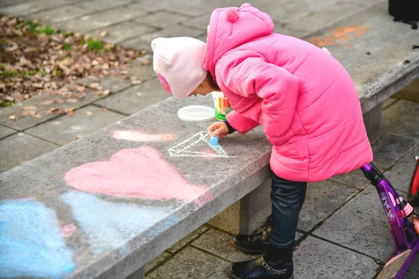 Девушка Розовой Куртке Рисует Сердца Карандашами Большой Бетонной Скамейке — стоковое фото