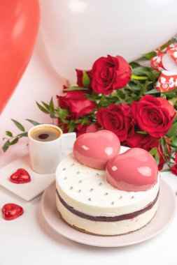 Beyaz jöleli kremalı kek, iki büyük pembe kalp, bir fincan kahve ve bir buket kırmızı gül.