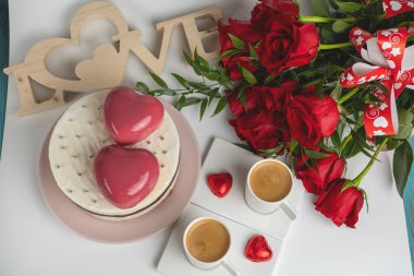 Beyaz jöleli kremalı kek, iki büyük pembe kalp, iki fincan kahve ve bir buket kırmızı gül.