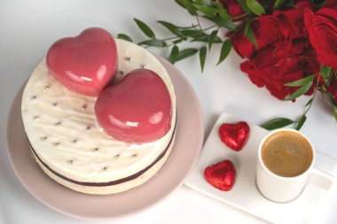 Beyaz jöleli kremalı kek, iki büyük pembe kalp, bir fincan kahve ve bir buket kırmızı gül.