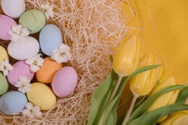 Samanlıkta çok renkli paskalya yumurtaları ve sarı arka planda sarı laleler.