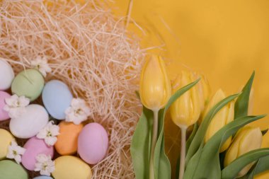 Samanlıkta çok renkli paskalya yumurtaları ve sarı arka planda sarı laleler.