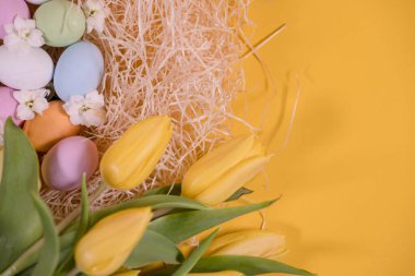 Samanlıkta çok renkli paskalya yumurtaları ve sarı arka planda sarı laleler.
