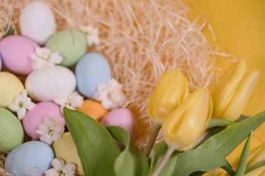 Samanlıkta çok renkli paskalya yumurtaları ve sarı arka planda sarı laleler.