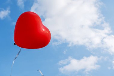 Mavi gökyüzü zemininde bulutlu kırmızı kalp şeklinde balon