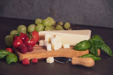 Domates, peynir, fesleğen, ahududu ve üzümler koyu arkaplanda zeytin tahtasında