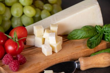 Domates, peynir, fesleğen, ahududu ve üzümler koyu arkaplanda zeytin tahtasında