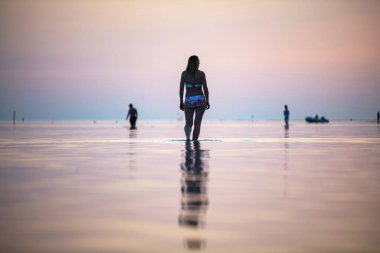 Gün batımında sahilde bir kız suyun üzerinde yürür.