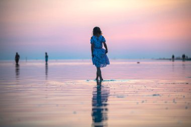 Gün batımında deniz kıyısında elbisesi olan bir kız suda yürür.