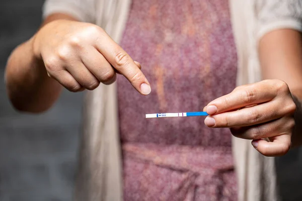 Gri bir arka planda elinde pozitif hamilelik testi tutan bir kız.