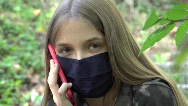 Больной ребенок носит защитную маску из-за пандемии коронавируса, ребенок разговаривает по смартфону в парке, девочка общалась по смартфону — стоковое видео