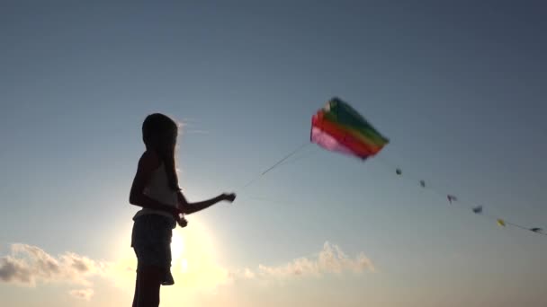 Dziecko bawiące się na plaży na wybrzeżu, dziecko latające latawcem o zachodzie słońca na oceanie, dziewczyna na linii brzegowej w letnie wakacje Fale morskie o zachodzie słońca — Wideo stockowe