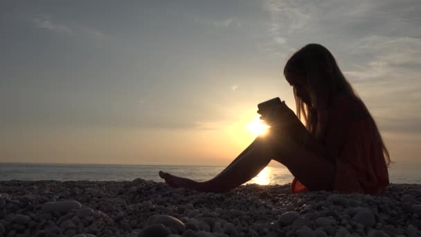 Dziecko grające na smartfonie, Dziecko na plaży o zachodzie słońca, Blondynka przeglądająca Internet na tablecie na wybrzeżu o zachodzie słońca, Wakacje letnie — Wideo stockowe