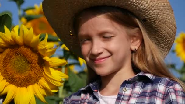 Портрет рільника в соняшнику, дитяче обличчя в сільському господарстві, що посміхається на фотоапараті, дівчина-ковбой грає на відкритому повітрі в природі. — стокове відео