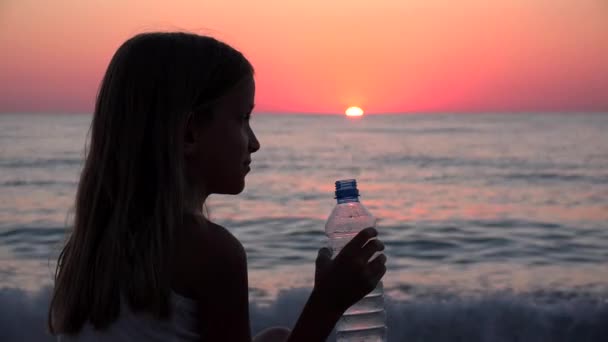 Dziecko pijące wodę na plaży o zachodzie słońca, Dziecko oglądające fale morskie na wybrzeżu, Dziewczyna na plaży, Wybrzeże — Wideo stockowe