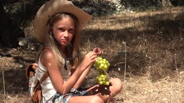 Kid Jedzenie winogron na łące, głodny rolnik dziecko zjada owoce, dziewczyna z kapeluszem kowboja relaks w sadzie oliwnym — Wideo stockowe