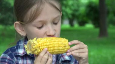 Çocuk parkta haşlanmış mısır yiyor, Aç Kız sağlıklı abur cubur yiyor, Genç Sarışın Çocuk doğada dinleniyor.
