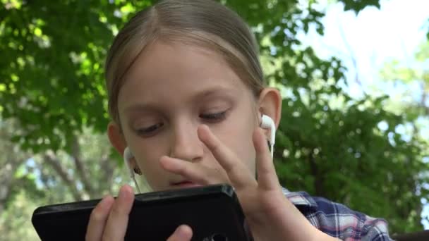 Kid Playing Tablet na placu zabaw w parku, Dziewczyna przeglądająca Internet, Dziecko używać smartfona na ławce odkryty w przyrodzie — Wideo stockowe