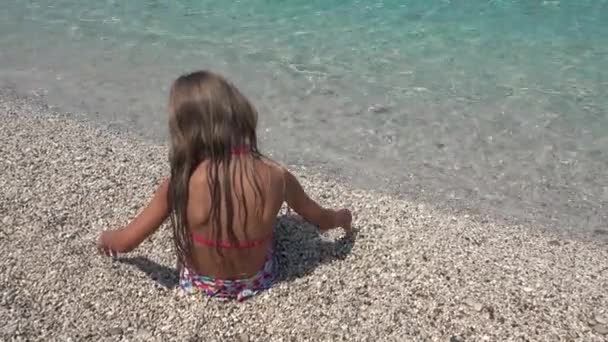 Dziecko bawiące się na plaży, Dziecko rzucające kamyczki w falach morskich na wybrzeżu, Dziewczyna oglądająca zachód słońca na wybrzeżu w wakacje — Wideo stockowe