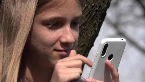 Kind spielt Smartphone an Baum, Teenager-Kind surft im Internet auf Smartphone im Park, Teenager-Mädchen auf Spielplatz — Stockvideo