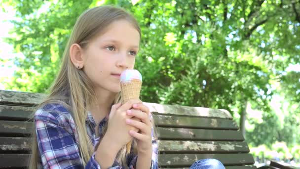 Παιδί τρώει παγωτό στο πάρκο, το παιδί χαλαρώνει κάθεται στο πάγκο, ξανθιά κορίτσι παίζει σε εξωτερικούς χώρους στην παιδική χαρά το καλοκαίρι — Αρχείο Βίντεο