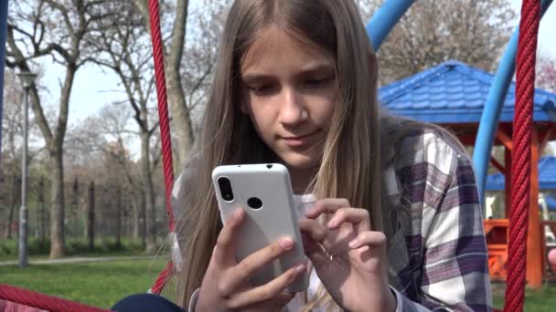 Teenager Kind spielt Smartphone, Kind surft im Internet auf Smartphone im Park, heranwachsende Mädchen benutzen Geräte im Freien auf Spielplatz — Stockvideo