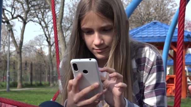 Adolescente niña jugando Smartphone, Niño navegar por Internet en el teléfono inteligente en el parque, Adolescente dispositivos de uso infantil al aire libre en el patio de recreo — Vídeo de stock